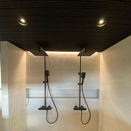 Kylpyhuoneessa musta katto ja vaaleat seinät sekä kaksi sadesuihkua vierekkäin