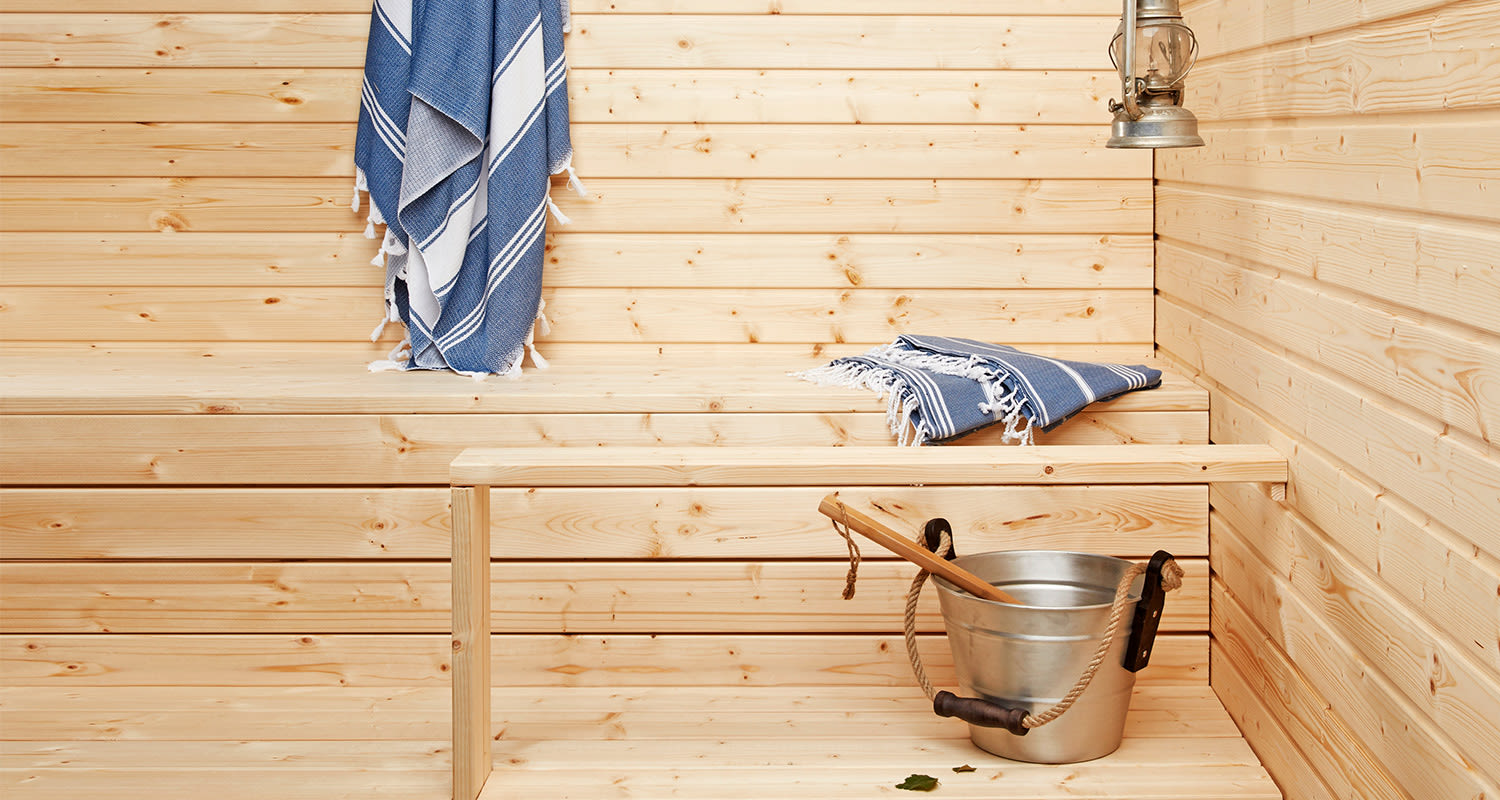 Vaaleapuisessa saunassa sinivalkoiset laudeliinat lauteilla, ämpäri kauhalla.