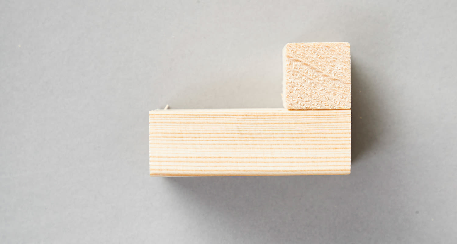 Kaksi vaaleaa puupalikkaa L-muodossa harmaalla taustalla.