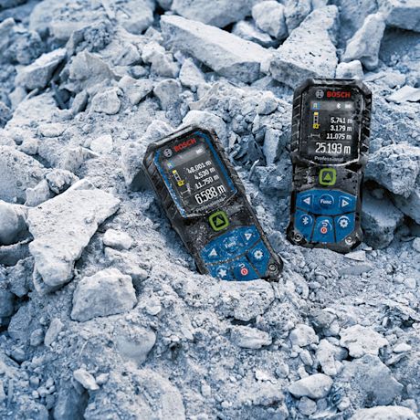 Kaksi Bosch-laseretäisyysmittaria kivenmurskahiekassa, kirkkaat näytöt päällä