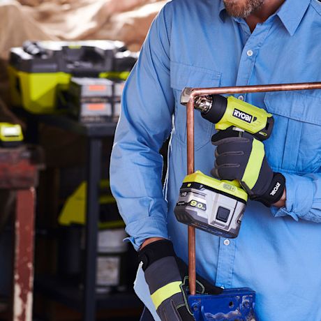 Mies sinisessä paidassa kiristää vihreällä ja mustalla Ryobi-akkuporakoneella kupariputkea.