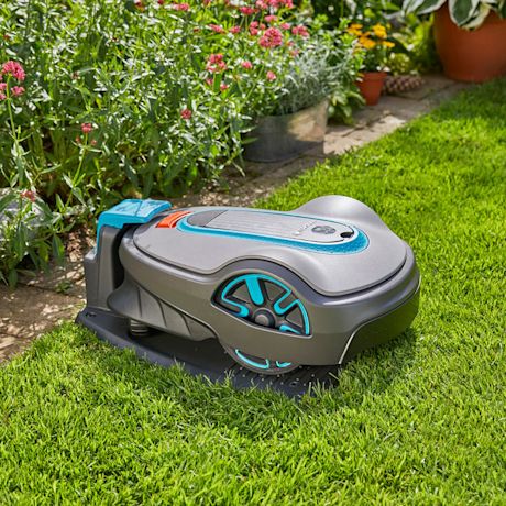 Harmaa-sininen robottiruohonleikkuri vihreällä nurmikolla kukkien vieressä