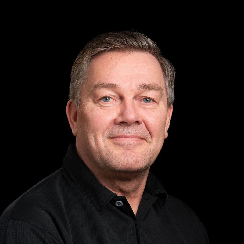 Keski-ikäinen mies pikeepaidassa, harmaat hiukset, mustalla taustalla.