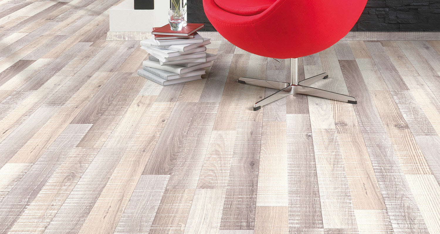 Punainen, pyöreä nojatuoli vaaleasävyisellä puulattialla, vieressä pinottuja kirjoja ja kukkavaasi.