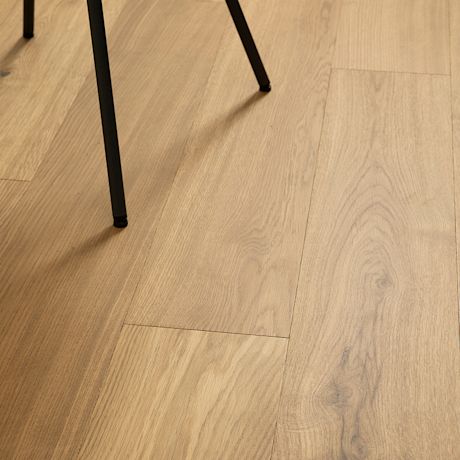 Kuvassa puunväristä kovetettua puulattiaa ja mustan tuolin jalat.