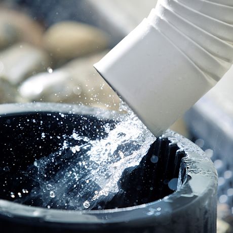 Valkoinen syöksytorvi valuttaa kirkasta vettä mustaan muovisäiliöön.