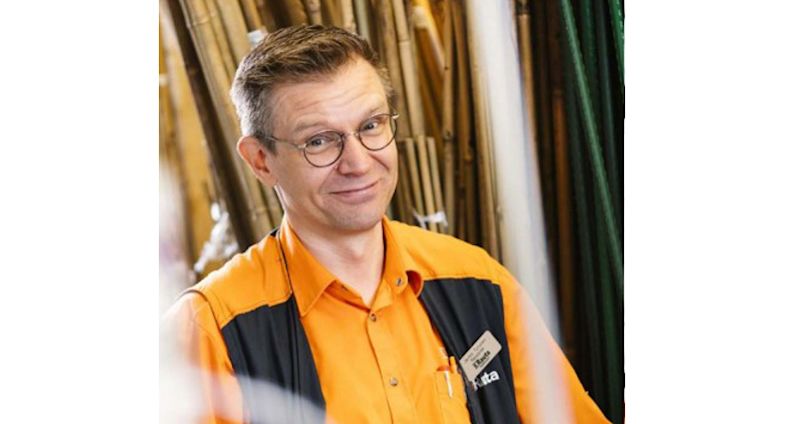 Rautakaupan työntekijä oranssi-mustassa työasussa pitkien putkien edessä