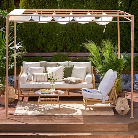 Terassilla pergola valkoisella kankaalla, valkoinen sohva ja nojatuoli tyynyin, viherkasveja.