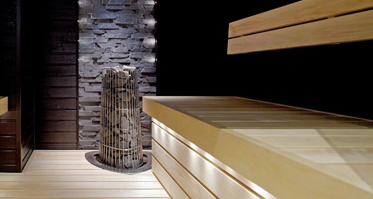 Moderni sauna, vaalea laude ja lattia, musta seinä, harmaa kiviseinä ja kiuas