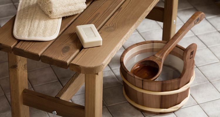 Ruskea puinen penkki saunahiomapadilla ja palasaippualla, vieressä puinen löylykiulu kauhalla.