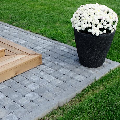 Musta ruukku täynnä valkoisia kukkia harmaalla pihakivellä ja vihreällä nurmikolla.