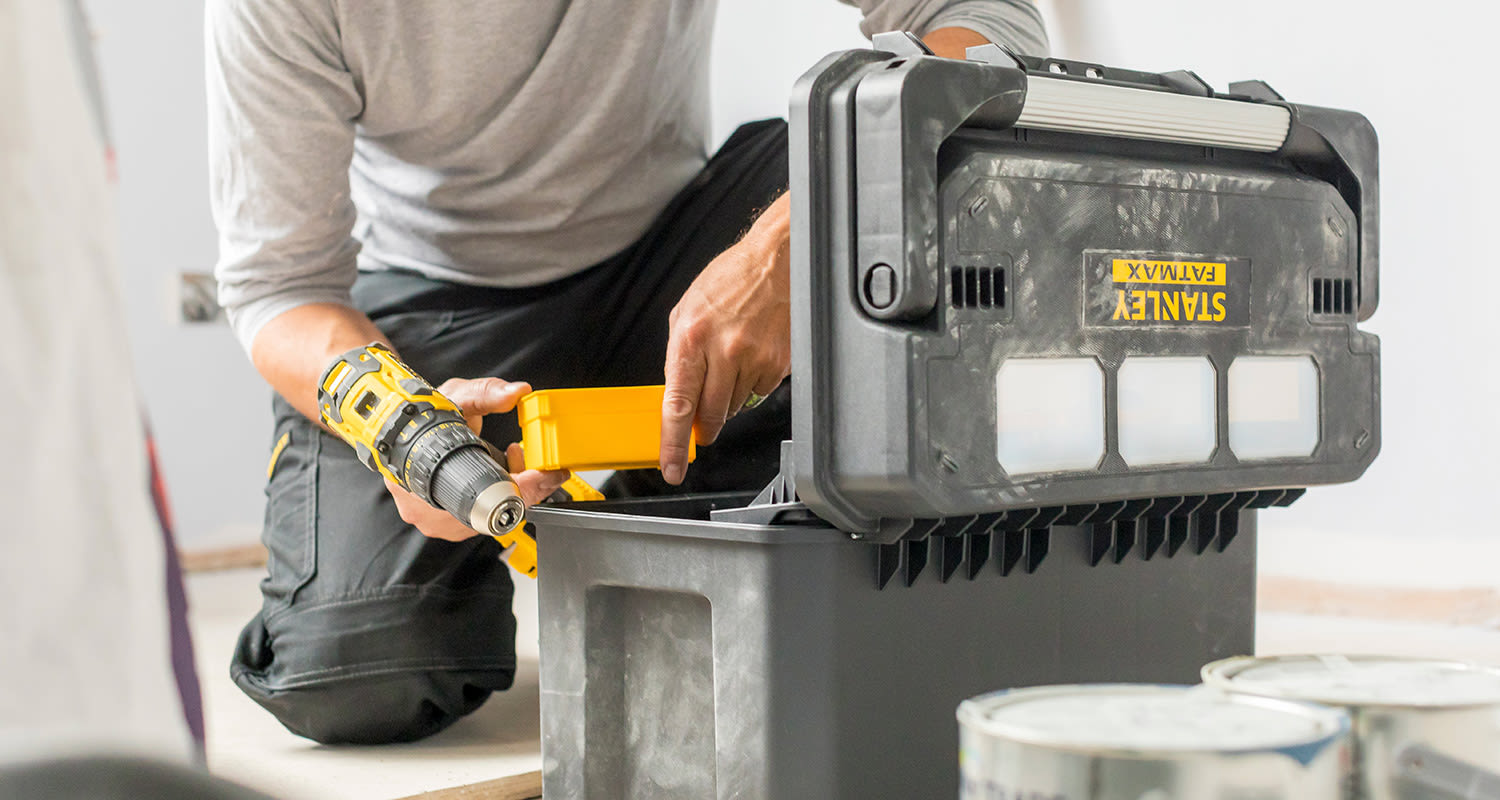 Mies asennushommissa Stanley-työkalupakin ja akkuporakoneen kanssa.