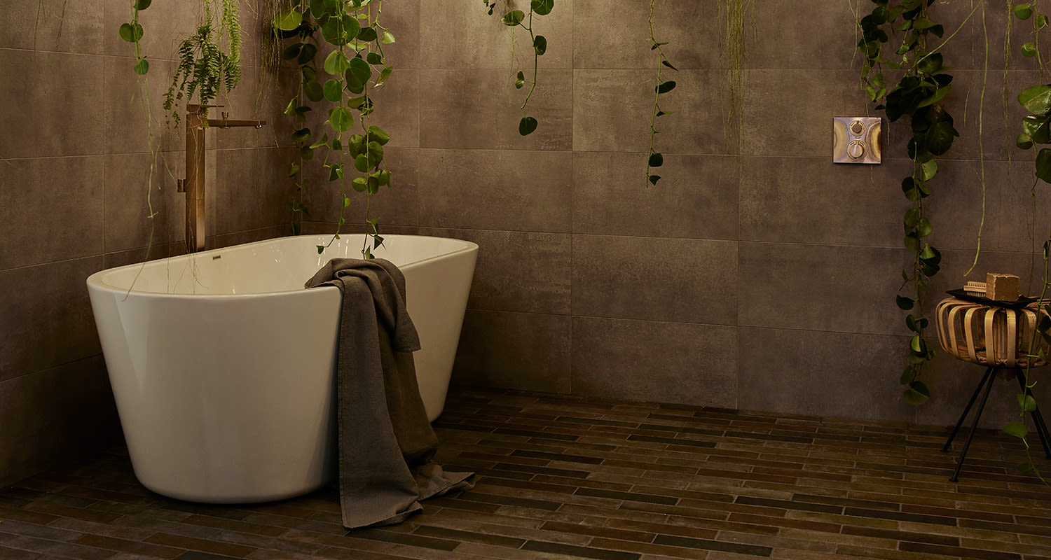 Harmaassa kylpyhuoneessa valkoinen irtoamme, roikkuvia vihreitä köynnöksiä ja tumma pyyhe.