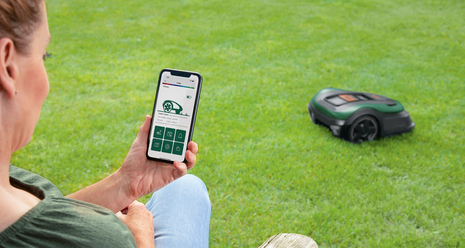 Älypuhelimen näytöllä robottiruohonleikkurin sovellus, leikkuri ajaa vihreällä nurmella.