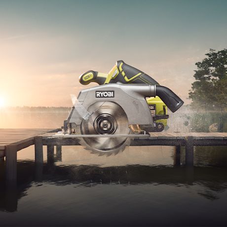 Vihreä-musta Ryobi-sirkkeli sahaamassa puulautaa laiturin yli järvimaisemassa auringonlaskussa