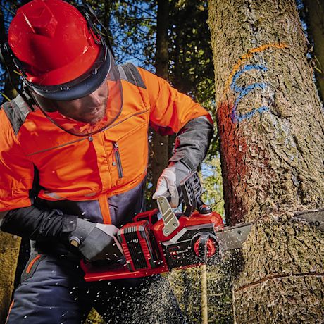 Oranssipukuinen sahaaja sahaa punaista moottorisahaa puunrunkoa jossa sininen ja oranssi merkki