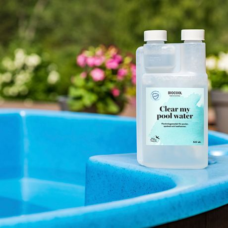 Biocool-kirkastusainepullo vaaleanturkoosilla etiketillä sinisen altaan reunalla, takana kukkia.