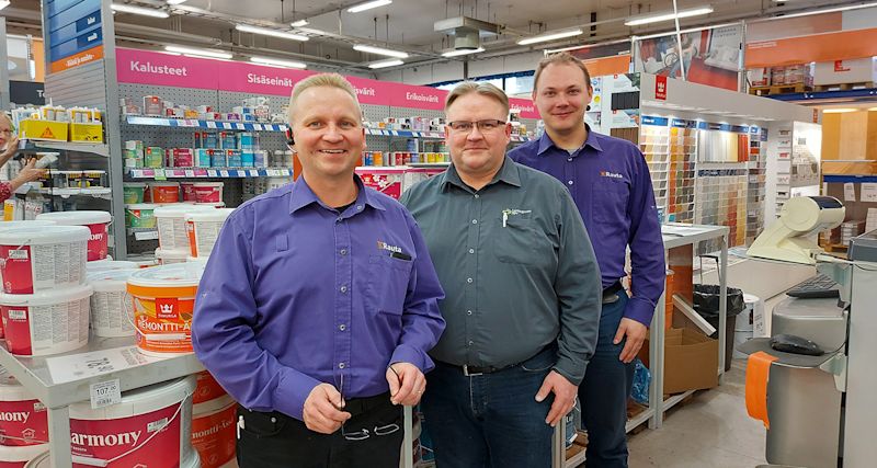 Kolme Rauta-myymälän työntekijää violeteissa ja harmaissa paidoissa maali- ja sisustusosastolla.