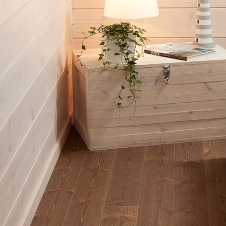 Vaalea puulaatikko nurkassa, valkoinen lamppu ja roikkuva viherkasvi tummaa puulattiaa vasten
