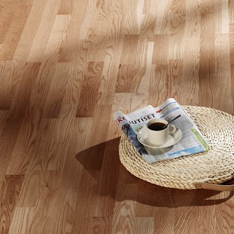 Vaalea puulattia, rottinkitarjotin, sanomalehti ja kupillinen mustaa kahvia