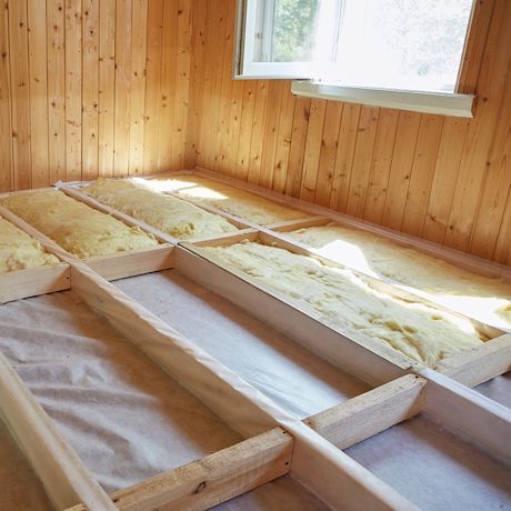 Hirsipaneliseinät ja avonainen ikkuna valaisevat lattian puujen väliin asennettua keltaista villaa.