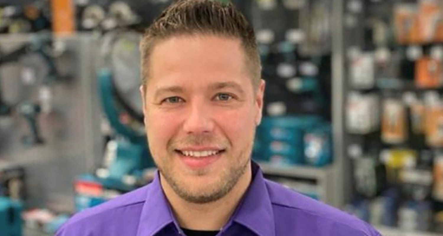 Mies violettipaidassa rautakaupan käytävällä sinisten työkalujen ja pakkausten edessä