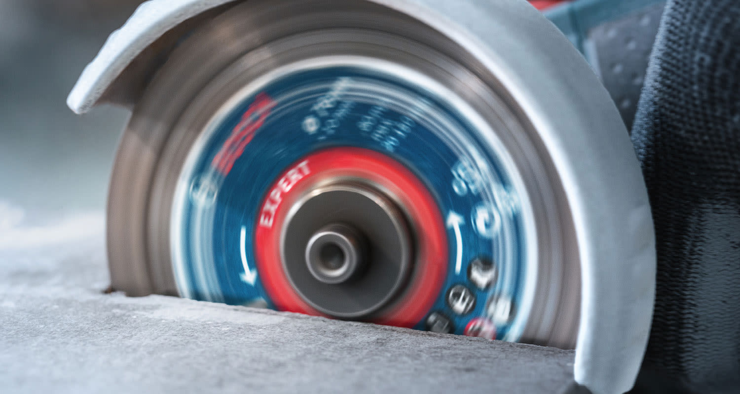 Punasininen ja sininen Expert-laikka pyörii ja leikkaa harmaata betonia