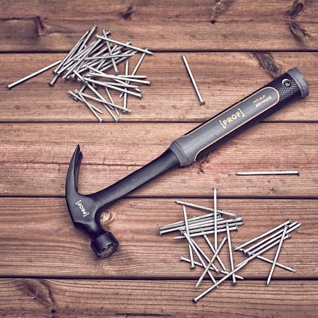 Musta keltareunainen vasara ja hopeanvärisiä nauloja tummanruskealla puulaudalla