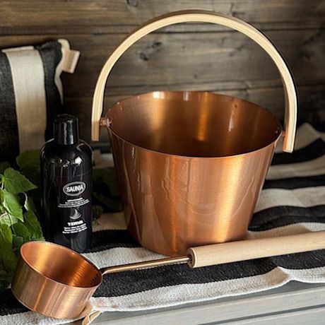 Kuvassa Saunian saunakiulu ja kauha sekä saunatuoksu raidallisen laudeliinan päällä.