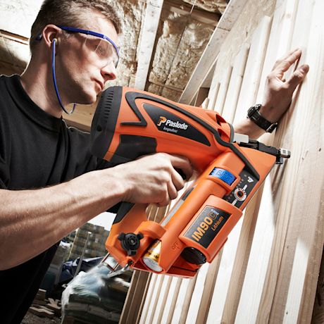 Rakennustyömies käyttää oranssinmusta Paslode IM90Ci -naulainta puuseinään sisätiloissa