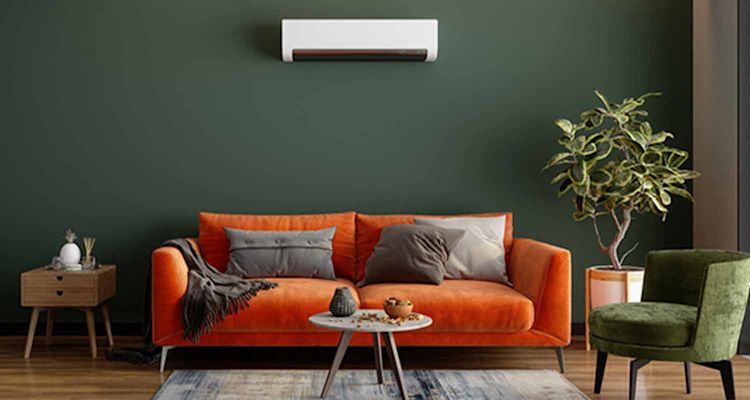 Oranssi sohva tummanvihreää seinää vasten, valkoinen ilmastointilaite, viherkasvi, vihreä nojatuoli.