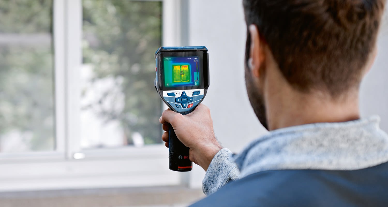 Mies pitää termovideokameraa ja mittaa ikkunan lämpövuotoa värillisellä näytöllä.