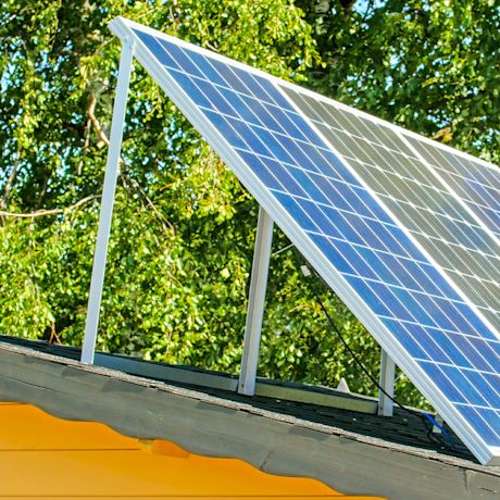 Kalteva sininen aurinkopaneeli keltaisen talon katolla, taustalla vihreät puut