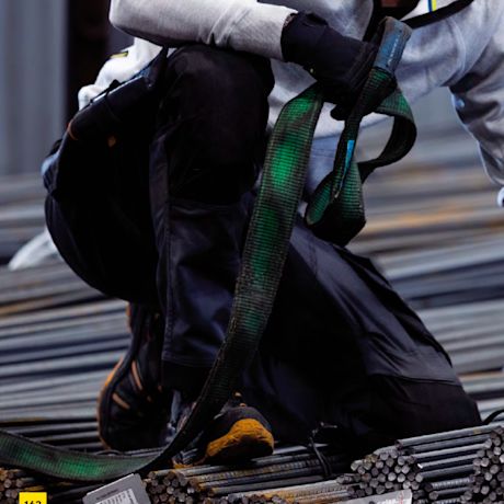 Kyykyssä oleva työvaatteinen henkilö pitelee vihreää turvavaljassilmukkaa terästangoilla.