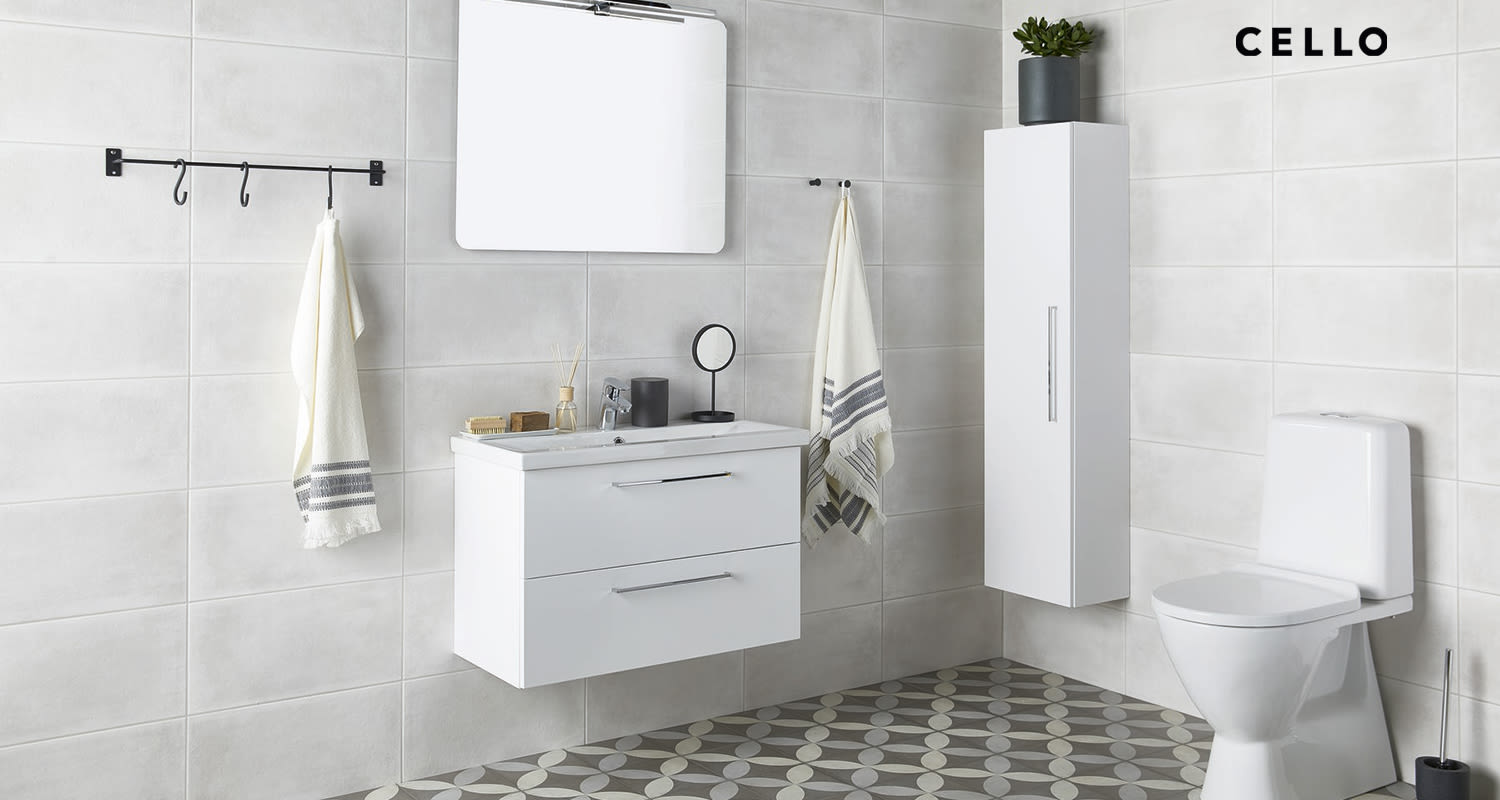 Kylpyhuone harmailla laatoilla, kuvioitu lattia, peili, valkoinen allas- ja pystykaappi sekä wc.