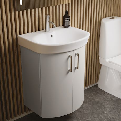 Valkoinen pyöristetty allaskaappi puupaneloitu seinä, vieressä WC ja musta saippuapullo