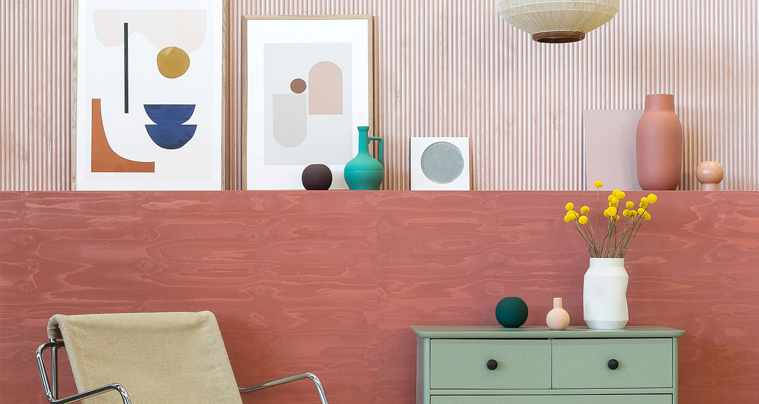 Vaaleanpunainen seinä, abstraktit taulut, mintuvihreä lipasto ja maljakko keltaisilla kukilla