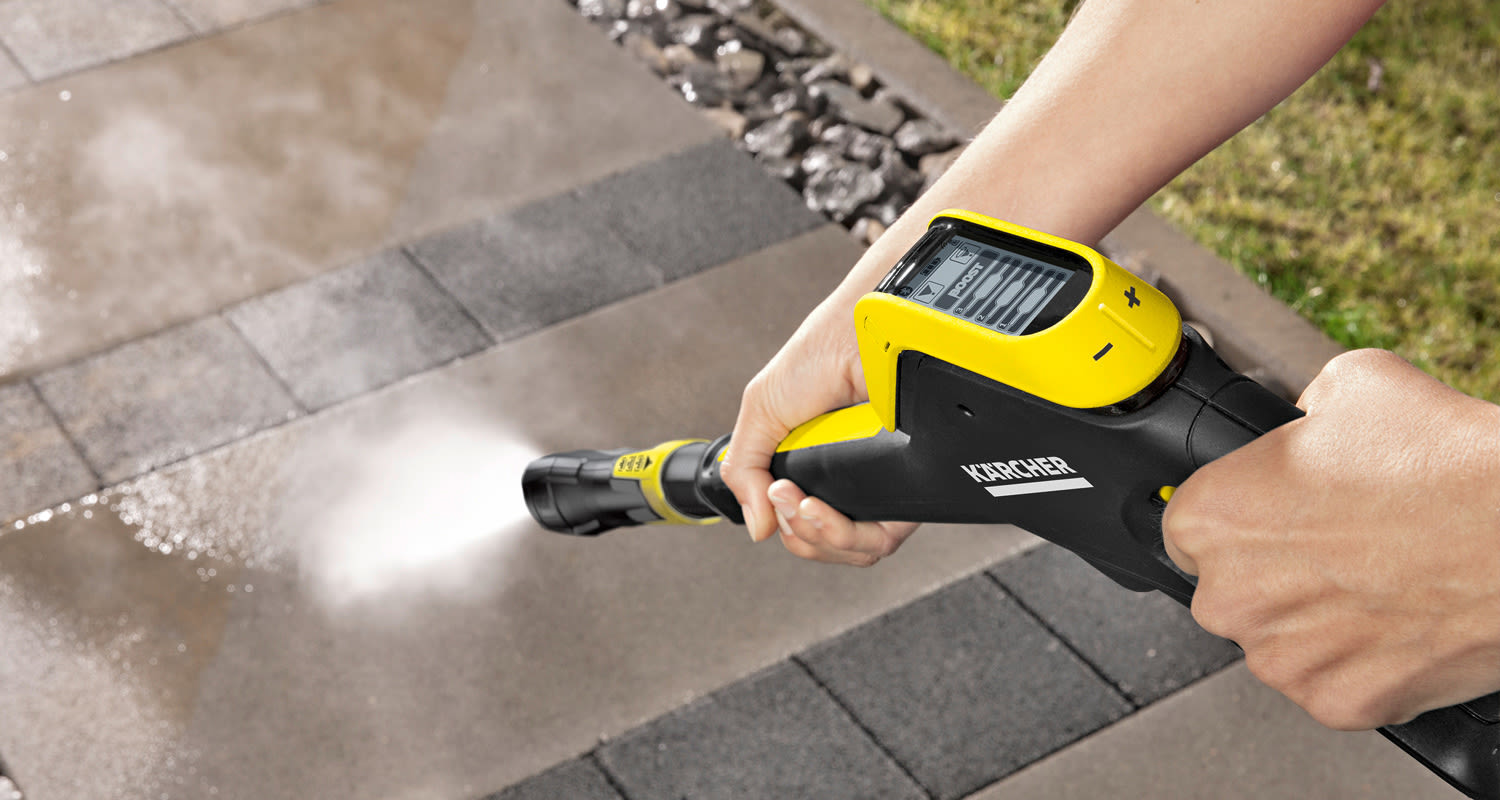 Keltamusta Kärcher-korkeapainepesuri suihkuttaa vesisuihkun harmaalle laattakivipinnalle