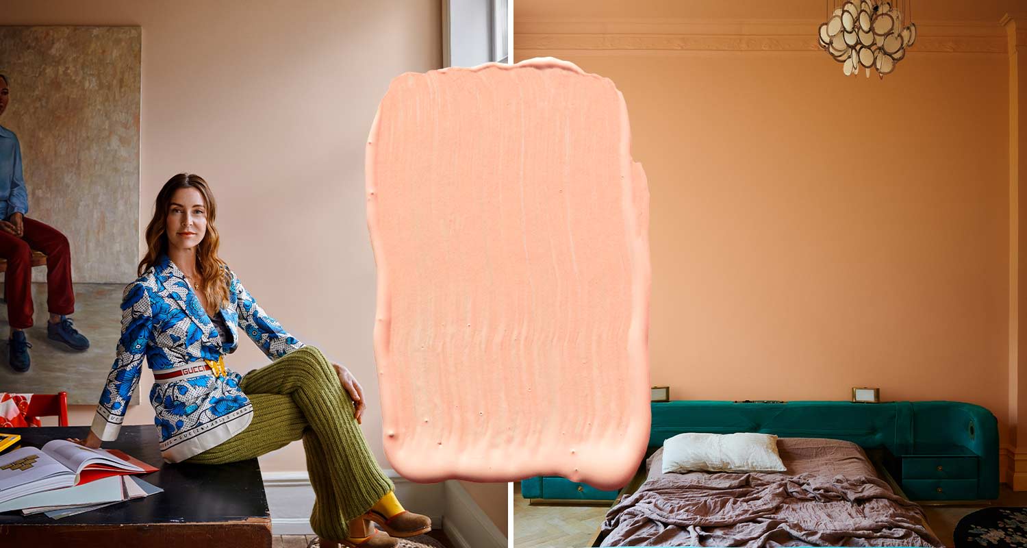 Siniseen kuosiin pukeutunut nainen pöydällä persikanvärisessä huoneessa, vihreä sängynpääty.