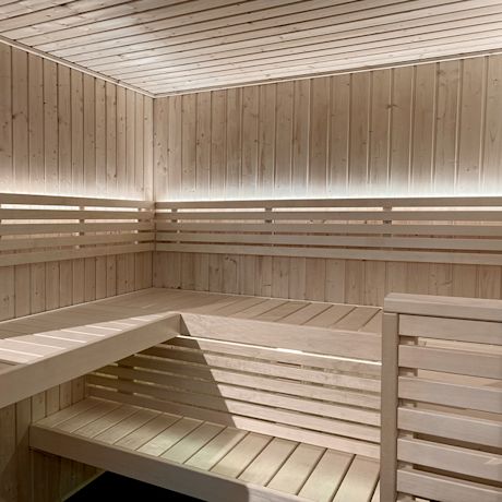 Vaalea kulmasauna vaaleasta puusta, himmeä LED-valaistus penkkien alla.