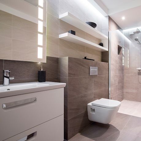 Moderni kylpyhuone vaaleanruskeilla laatoilla, valkoinen allaskaappi, seinä-wc ja lasinen suihku