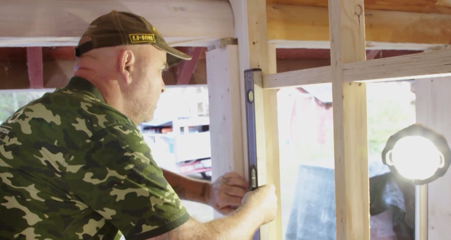 Mies camokuosisessa paidassa mittaa puurunkoa vesivaa’alla valovoimaisen työvalon vieressä