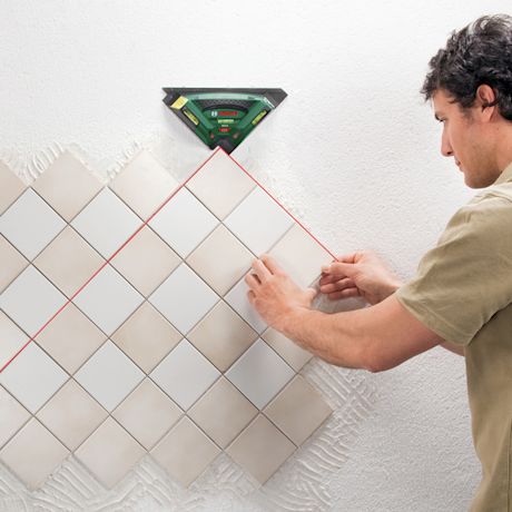 Mies kiinnittää vaaleita neliölaattoja diagonaaliasennuksessa seinälle laserlinjalaitteella.