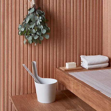 Saunan puupaneeliseinä, ripustettu eukalyptus, valkoinen löylykiulu, pyyhkeet ja saippua.