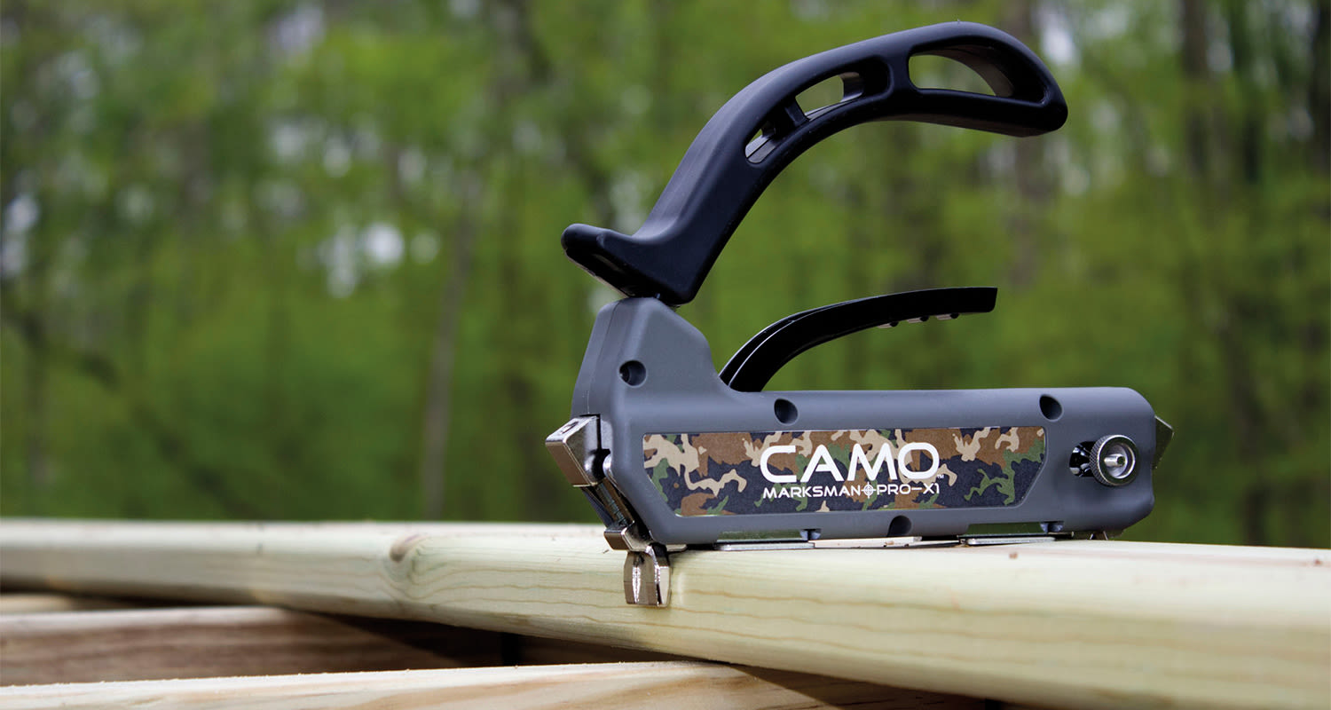 Harmaan ja mustan CAMO Marksman Pro-X1 -naulain vaalealla puulaudalla vihreän metsän edessä