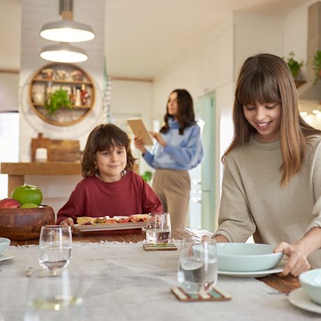 Lapset kattavat kotona ruokapöytää äidin säätäessä huoneeseen sopivaa valaistusta kattovalaisimista