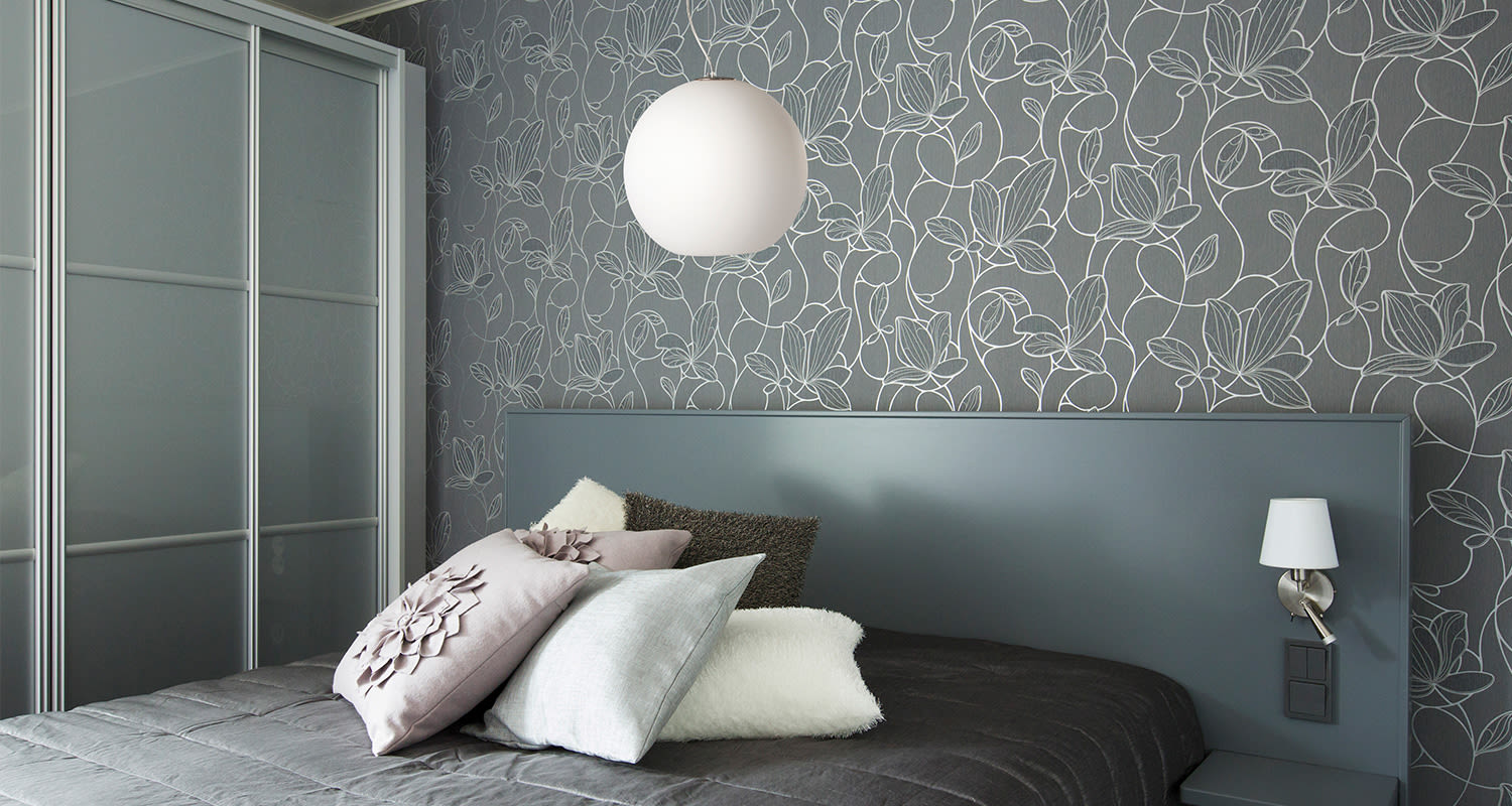 Moderni harmaa makuuhuone, valkoisella kukkakuvioidulla tapetilla ja pastellisävyisillä tyynyillä.