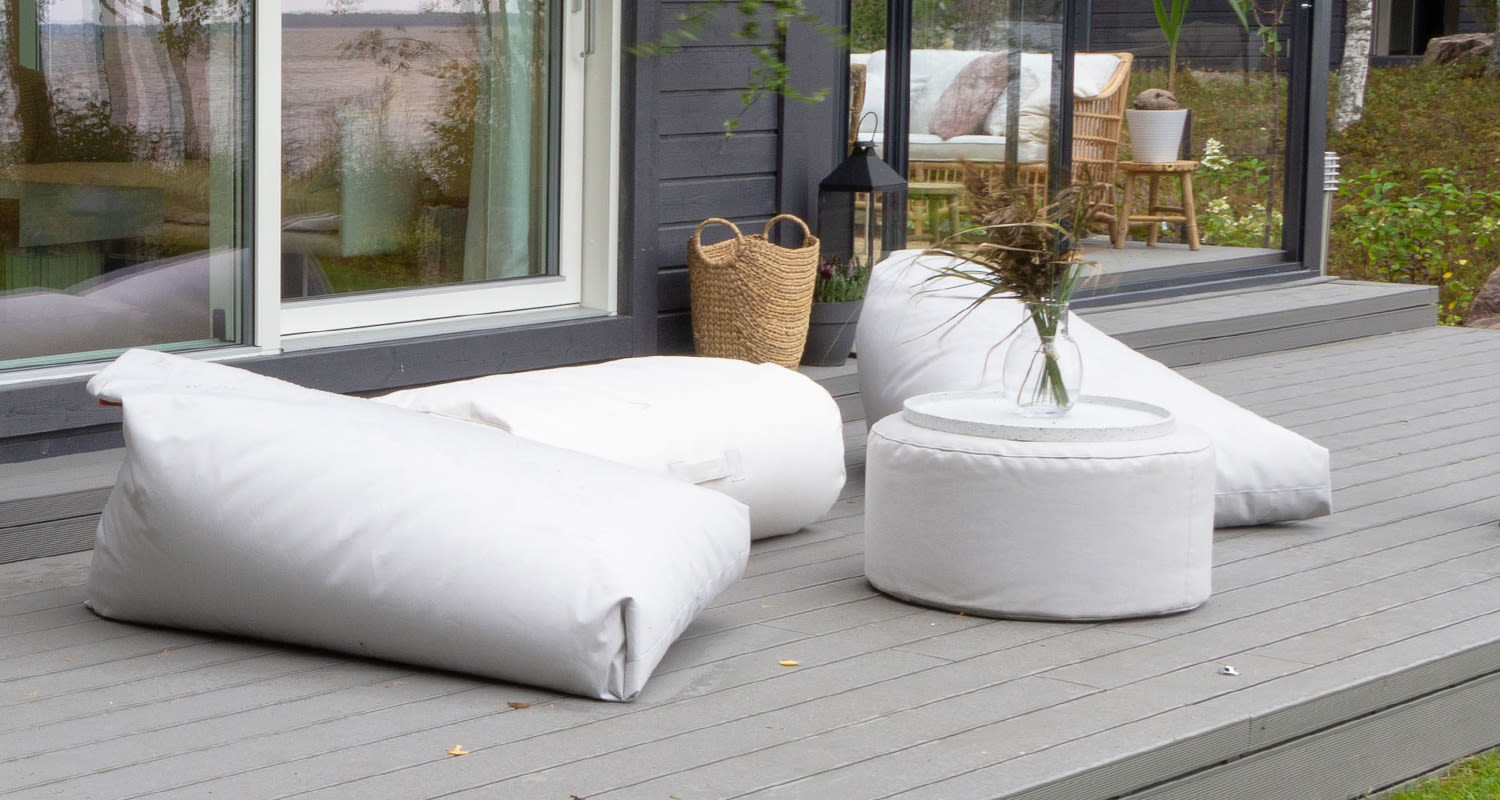 Harmaalla terassilla valkoiset säkkituolit ja pyöreä pöytä, ikkunoista järvimaisema.