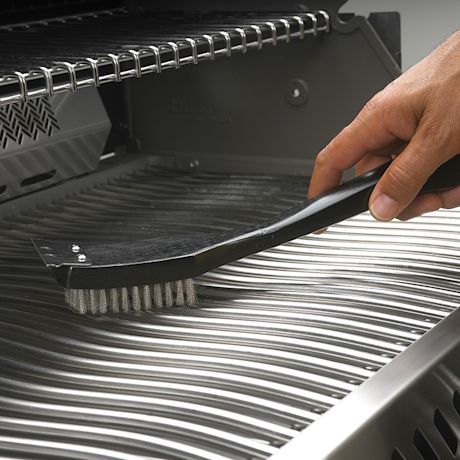 Käsi puhdistaa mustalla harjalla ruostumattoman teräksen grilliritilää.