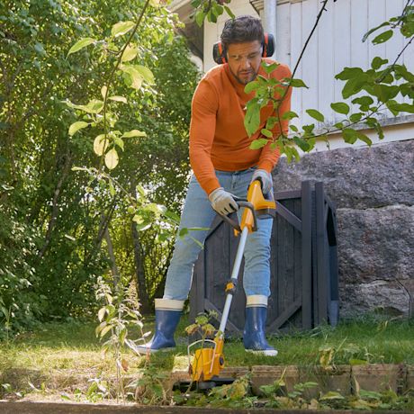 Henkilö oranssissa paidassa ja sinisissä saappaissa ruohonleikkurilla vihreässä puutarhassa.